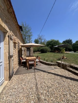 Terrasse privée avec table en bois et parasol devant la bâtisse en pierres traditionnelles à Le Coux-et-Bigaroque