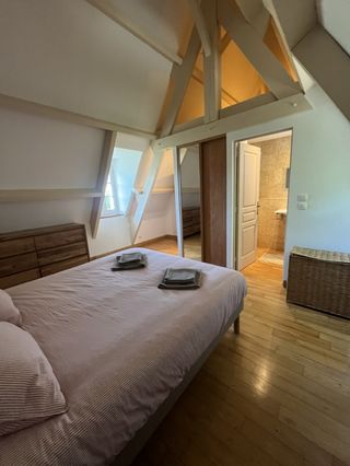 Chambre parentale mansardée avec grand lit double, charpente apparente et parquet au gîte Lou Cantou en Dordogne
