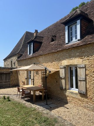 Terrasse aménagée pour repas en extérieur au pied d'un gîte de charme en pierre blonde du Périgord