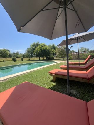 Transats rouges à l'ombre d'un parasol au bord de la piscine du gîte pour un séjour farniente